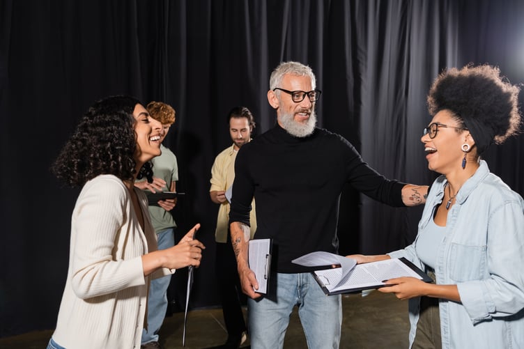 cheerful african american woman holding screenplay and laughing near bearded producer and multiethnic actors in theater,stock image