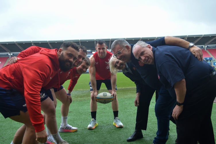 Scarlets scrum-half Gareth Davies feeds a scrum with some of the Scarlets squad taking on a front row of (L-R) Captain Karen Symonds of The Salvation Army in Llanelli, Scarlets Stadium Manager Dave Healey and the manager of The Salvation Army charity shop in Llanelli Antony Chappell