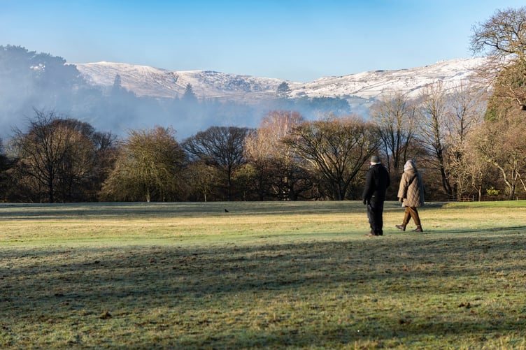 Visitors walking in the grounds of Bodnant Garden, Conwy, Wales, with snow covered Carneddau mountains of Eryri (Snowdonia) behind.